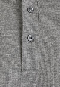 Grå pikétröja i tyg med texturerad finish, med tre svarta knappar och en liten, sydd krage.