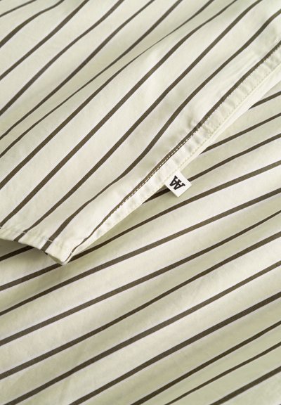 Tissu rayé jaune pâle avec des fines lignes verticales brun foncé. Comprend une petite étiquette blanche avec des initiales dans un coin.