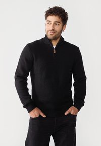 Sudadera negra con cremallera en punto texturizado, con mangas largas, puños acanalados y una cremallera prominente con un acento marrón.
