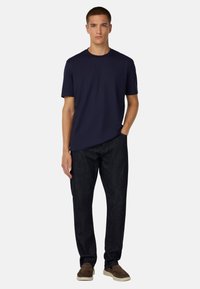 Námořnické tričko s krátkým rukávem v kombinaci s tmavými džíny a hnědými slip-on botami. Klasický střih s volným fit a hladkou texturou.