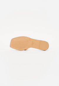 Beige høyhælte sandaler med et slankt design, teksturert såle og firkantet tå. Har åpen bakdel og en minimalistisk stropp over foten.