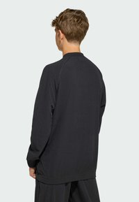 Black ribbed long-sleeve top with raglan sleeves and a relaxed fit. Features a subtle texture and plain design, no visible logos or accents.
