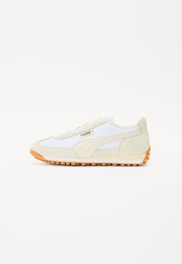 Baskets blanches de sport en daim et mesh, avec une semelle en caoutchouc caramel et un logo discret en or. Design rétro classique.