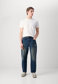 Hvid crew-neck t-shirt parret med løst siddende blå denim jeans. Sneakers med grønne accenter. Glat stof med let falmning på jeans.