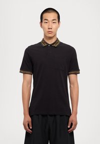 Čierna polo košeľa s vreckom, s motívovaným golierom a manžetami v zlatej a čiernej farbe, vyrobená z hladkého bavlneného zmesi.