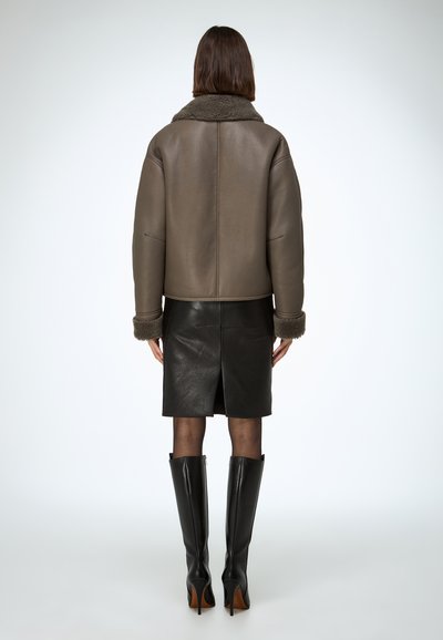 Hnedá kožená bunda s kožušinovým golierom, so štruktúrovaným strihom a žebrovanými manžetami. Kombinovaná s čiernou koženou sukňou a čiernymi čižmami po kolená.