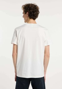 Camiseta de algodón blanca con mangas cortas, corte relajado y diseño sencillo. La vista trasera muestra un escote redondo y una textura suave.