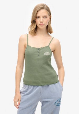 Zielony, prążkowany top na ramiączkach z koronkowym wykończeniem, z guzikami i nadrukiem logo. Połączony z jasnoszarymi, luźnymi spodniami dresowymi.