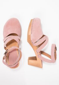 Rosa Wildleder-High Heels mit gekreuzten Riemen und einem Holzabsatz. Sie verfügen über eine runde Zehenpartie und einen Schnallenverschluss an einem Riemen.