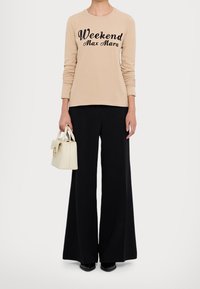 Beige Langarmshirt mit schwarzem "Weekend Max Mara"-Schriftzug, kombiniert mit schwarzen weiten Hosen und einer kleinen cremefarbenen Handtasche.