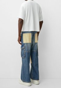 Vit kort t-shirt, denim cargo-byxor med gula lappfickor, vida ben, ljusblå tvätt och detaljer i sömmarna. Stylat med vita sneakers.