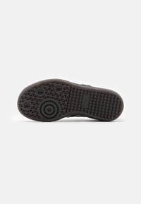 Black rubber shoe sole featuring a textured grip pattern, circular and oval accents, with a central branded logo area.