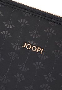 Clutch nera con motivo floreale a rilievo, logo dorato "JOOP!" in evidenza, dotata di cerniera testurizzata e materiale in tessuto.