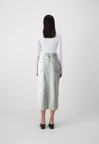 Lysvasket denim midi-skjørt med tettsittende midje, sidelommer og rett snitt. Kombinert med en tettsittende hvit langermet topp.
