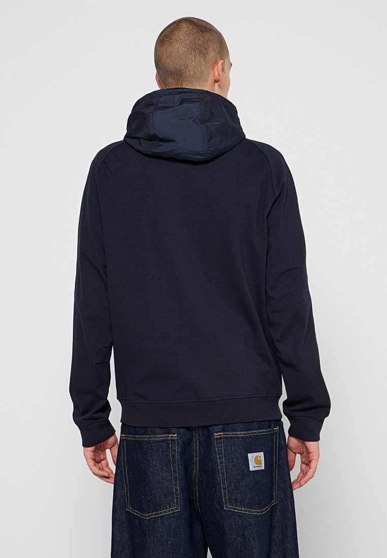 Haut à capuche bleu marine avec une capuche matelassée, un cordon de serrage, et des poignets et un ourlet côtelés. Fabriqué en tissu doux, avec une coupe décontractée.