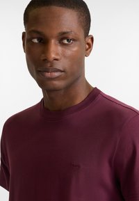 Burgundy crew-neck t-shirt made of smooth cotton blend, featuring short sleeves and a small embroidered logo on the chest.