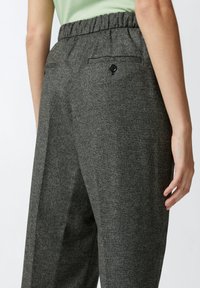 Sive tkanine hlače s elastičnim pojasom, s stražnjim džepom s crnim gumbom i glatkom teksturom.