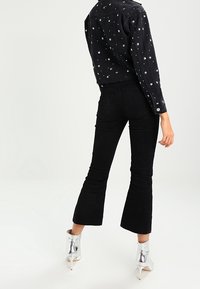 Černá džínová bunda s bílým hvězdným vzorem, spárovaná s černými rozšířenými džíny. Modelka nosí reflexní stříbrné kotníkové boty.