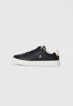 Sort læder-sneaker med hvid sål, hvid hæl-accent, sorte snørebånd og lille guldlogo på siden.