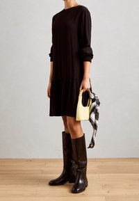 Vestido negro de manga larga con dobladillo fruncido, botas de cuero negras hasta la rodilla y un pequeño bolso amarillo con una bufanda estampada.