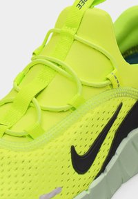 Φωτεινό νέον κίτρινο αθλητικό παπούτσι με μαύρο λογότυπο Nike, ελαστικά κορδόνια με θηλιά και αναπνεύσιμο επάνω μέρος από δίχτυ, σε κοντινή λήψη.