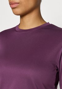 Violetti, pitkähihaisen paidan tekstuuri, jossa pyöreä pääntie. Kankaassa on hillitty kuvio ja sileä viimeistely.