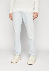 Jeans de mezclilla azul claro con un corte recto, un desvanecimiento sutil y costuras en contraste, combinados con zapatillas blancas y un suéter blanco texturizado.