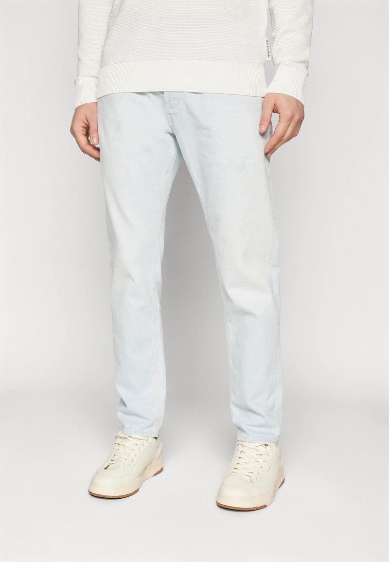 Jeans de mezclilla azul claro con un corte recto, un desvanecimiento sutil y costuras en contraste, combinados con zapatillas blancas y un suéter blanco texturizado.