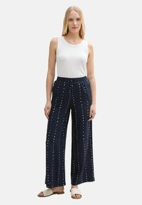 Navy wide-leg pants with white polka dot pattern, elastic waistband, and drawstring. Paired with a fitted white tank top and sandals.