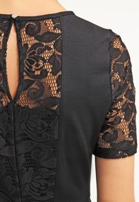 Czarna sukienka z koronkowym tyłem i rękawami z kwiatowym wzorem, z zapięciem w kształcie łezki na szyi oraz gładkim materiałem.