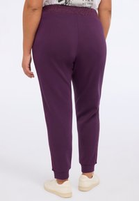 Lila Jogginghose mit glitzerndem Bund und seitlichen Akzenten, mit schmal zulaufendem Bein und Rippbündchen, aus weichem, dehnbarem Material.