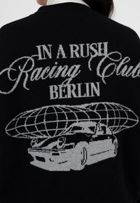 Czarny sweter dzianinowy z srebrnym wyszywanym napisem "IN A RUSH Racing Club BERLIN" oraz grafiką samochodu pod globusem.