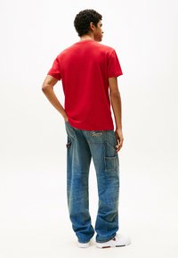 Rotes Kurzarm-T-Shirt mit einem runden Ausschnitt. Kombiniert mit einer lockeren blauen Jeans-Cargohose mit Taschen und Markenakzenten.