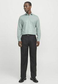 Lichtgroen overhemd met knopen, lange mouwen, met zwarte dresspants. Een zwarte riem en schoenen maken de outfit compleet, wat een formele uitstraling benadrukt.