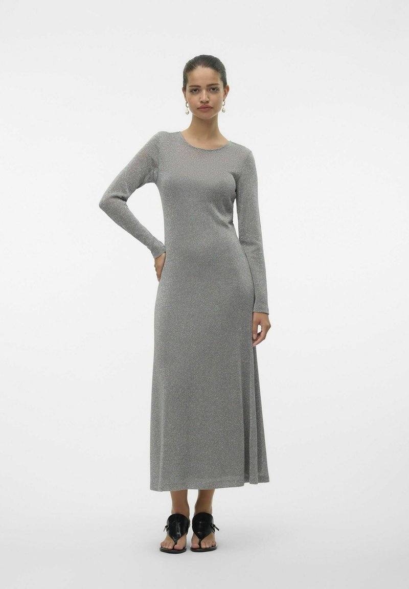 Långärmad grå stickad klänning med en åtsittande överdel och en utsvängd kjol, med rund halsringning och en mjuk, texturerad ytfinish. Bärs med svarta sandaler.