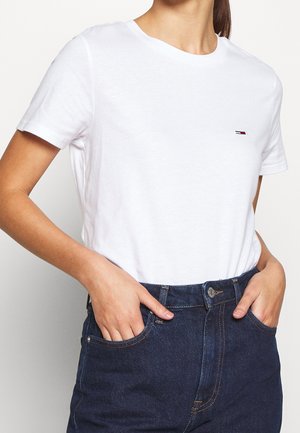 Wit katoenen T-shirt met een ronde hals, korte mouwen en een klein logo in rood, wit en blauw op de borst. Gecombineerd met donker denim.