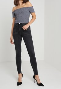 Top de hombros al descubierto, azul marino con un patrón floral; combinado con jeans ajustados negros y tacones altos negros, con un diseño ajustado.