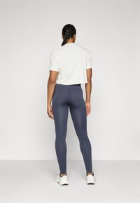 T-shirt bianco accorciato e leggings a coste blu scuro, abbinati a sneaker bianche. L'outfit presenta un design aderente e elasticizzato.