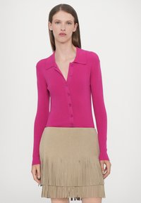 Cardigan ribbed fucsia cu guler și închidere cu nasturi, purtat cu o fustă din suede bej cu franjuri.