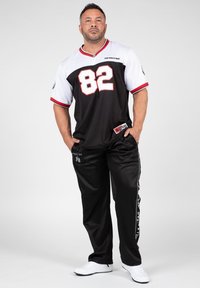 Camiseta negra con mangas cortas blancas y acentos rojos, que lleva el número 82. Pantalones negros con rayas laterales y zapatos blancos.