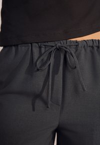 Pantaloni grigio scuro a gamba larga realizzati in un tessuto morbido e strutturato. Presentano una vita elasticizzata con coulisse annodata e tasche laterali.