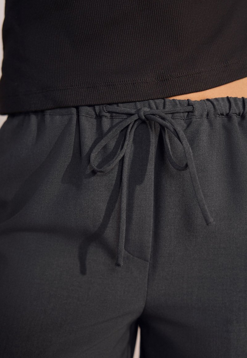 Pantaloni grigio scuro a gamba larga realizzati in un tessuto morbido e strutturato. Presentano una vita elasticizzata con coulisse annodata e tasche laterali.