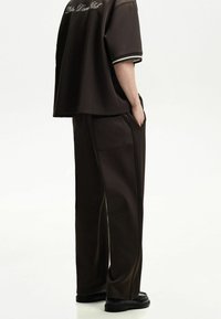 Mörkbrun oversize t-shirt med korta ärmar och vita detaljer, kombinerad med mörkbruna vida byxor med sidofickor.