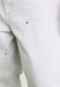 Light gray trousers with a textured finish, featuring gold hardware accents on the pockets and subtle stitching details.