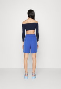 Námořnická off-the-shoulder blůza spárovaná s modrými šortkami. Blůza je přiléhavá s dlouhými rukávy a šortky mají elastický pas.