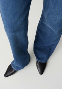 Wijd uitlopende blauwe denim jeans gecombineerd met zwarte leren hakken met puntige neus. De denim heeft een klassieke wassing met subtiele vervaaging.