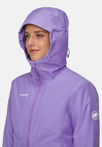 Chaqueta impermeable de color púrpura claro con capucha ajustada, cremallera frontal y logotipo en el pecho. Textura suave con un acabado ligeramente brillante.