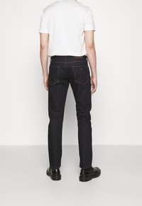 Mörka denimjeans med avsmalnande ben, kontrastsömmar och två bakfickor. Bärs med en enkel vit t-shirt och svarta skor.