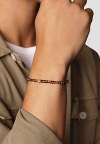 Beaded bracelet featuring multicolored glass beads in amber and brown tones, with a small gold accent bead. Worn on a wrist.