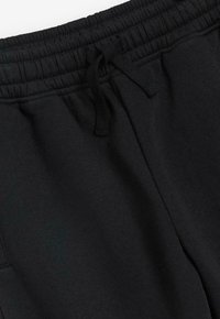 Sorte sweatpants med elastisk talje, der har snor og en glat tekstur, lavet af et blødt materiale. Ingen synlige mønstre eller accenter.
